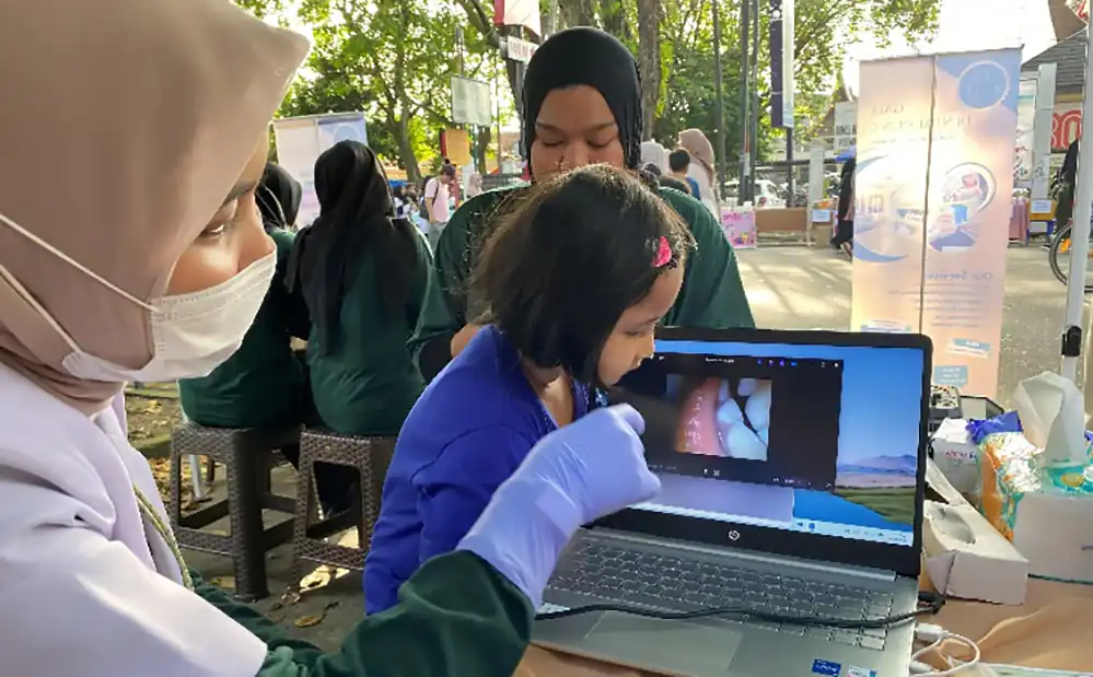 Petugas GAIA Dental Clinic memberikan penjelasan mengenai kondisi kesehatan gigi kepada seorang anak melalui tampilan layar laptop dalam kegiatan pemeriksaan gratis di Car Free Day (CFD) Padang, Minggu (26/4/2026). Penggunaan teknologi kamera intraoral ini bertujuan memberikan pemahaman visual secara langsung kepada warga agar lebih peduli terhadap kesehatan mulut sejak dini.